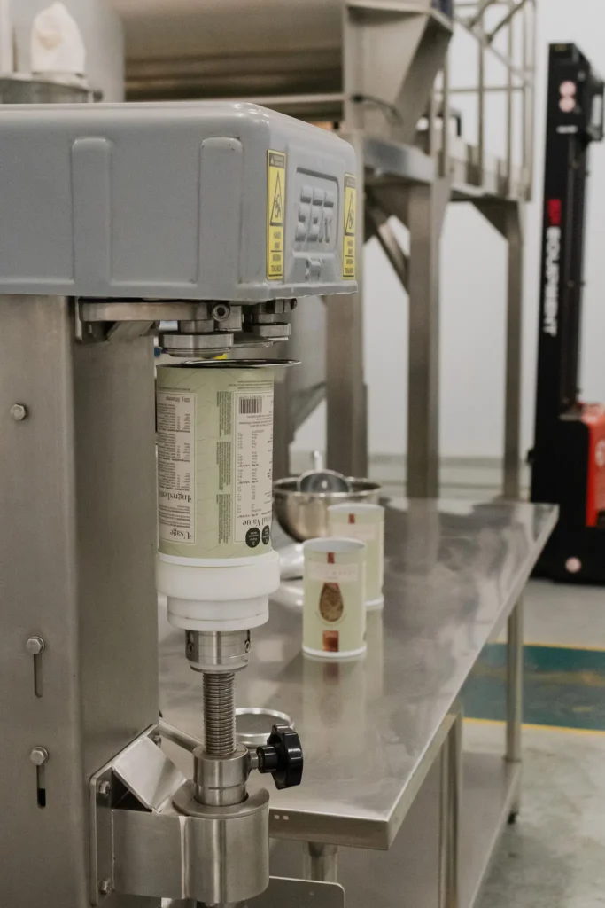 A labelled supplement tub being filled with powder at the dosing head of the filling machine